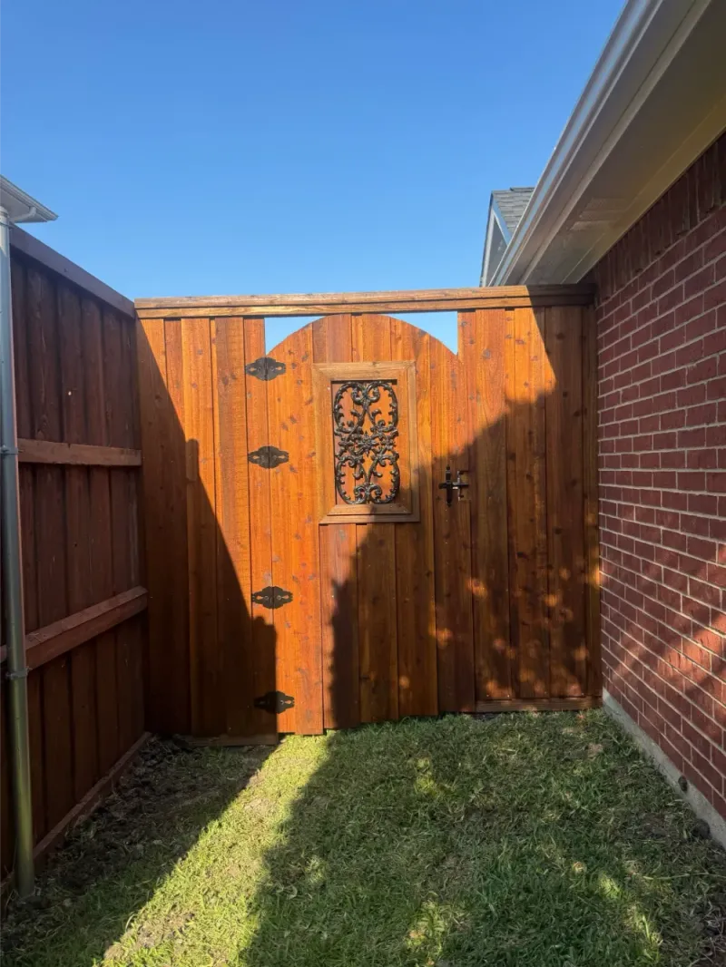 An arched cedar gate with an iron scrollwork insert set into a board-on-board run.