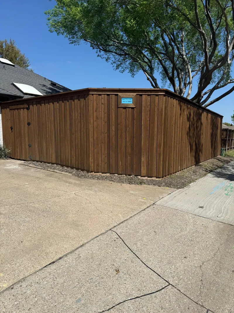 A pre-stained board-on-board fence with a top cap at a driveway corner, company sign visible.