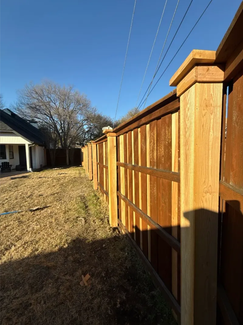 A cedar privacy fence with post caps along a property line.