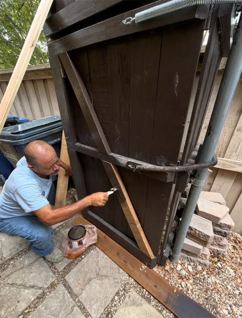 A crew member kneeling to repair and restain a gate brace.