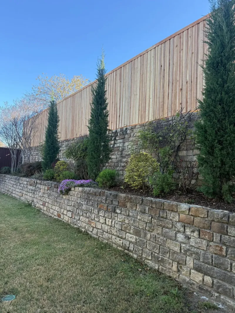 A close view of a finished wood fence run with its top cap, meeting a stone wall.
